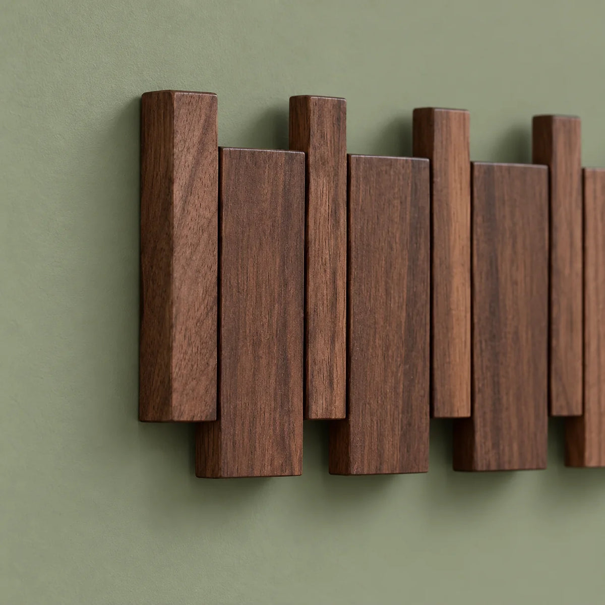 Détail de l’extrémité gauche du porte-manteau compact en bois foncé sur fond vert