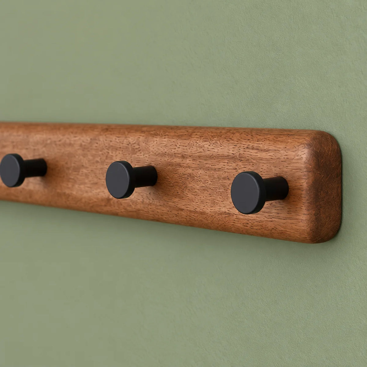 Détail de l'extrémité arrondie en bois et des crochets noirs sur fond vert