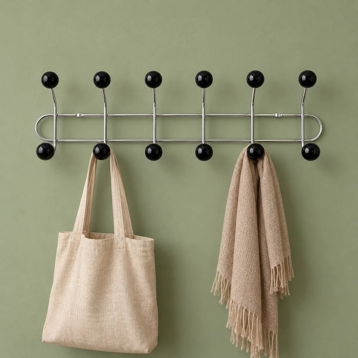 Porte-manteau mural à boules noires avec sac en lin et écharpe sur fond vert
