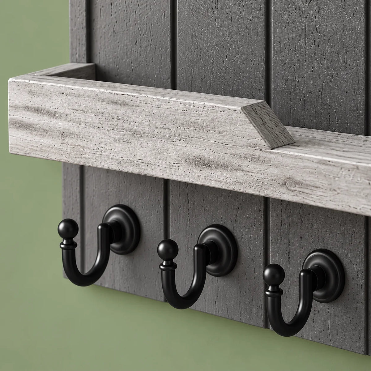 Détail du panneau gris, du rebord clair en angle et des crochets noirs sur fond vert sauge