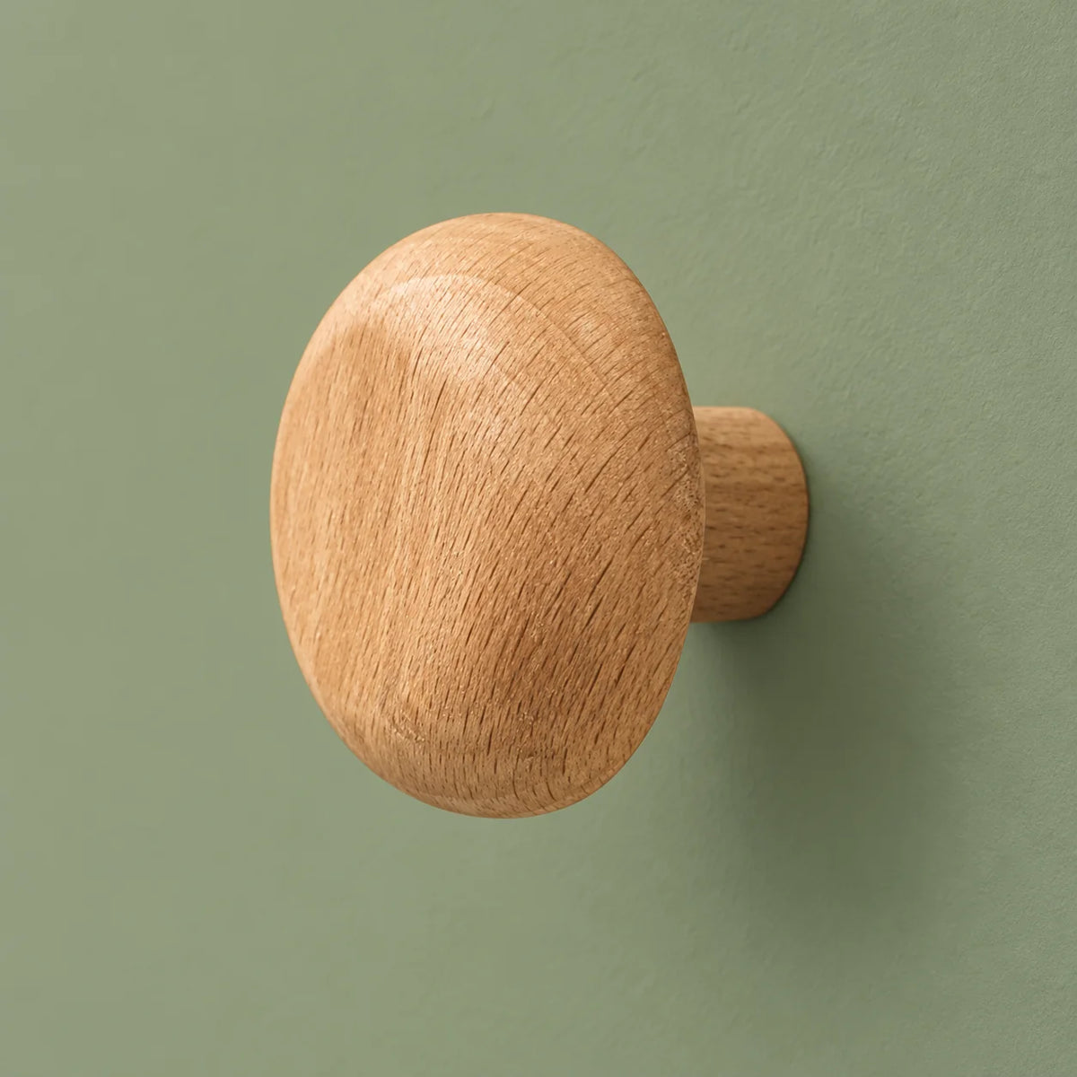 Patère ronde en bois clair vue de trois quarts sur fond vert sauge