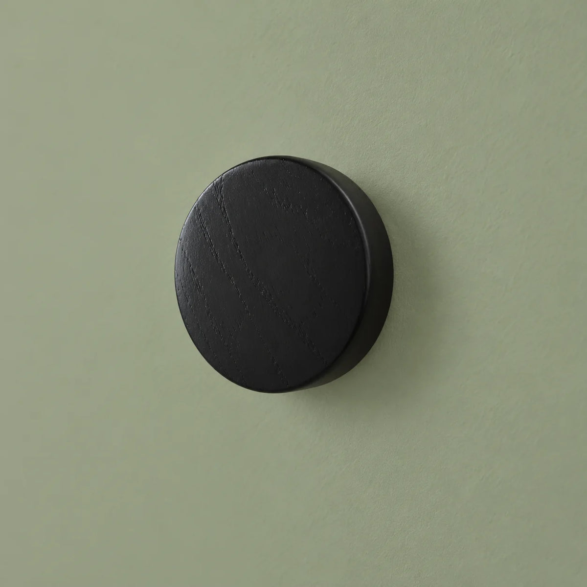 Patère ronde noire vue de trois quarts sur fond vert sauge