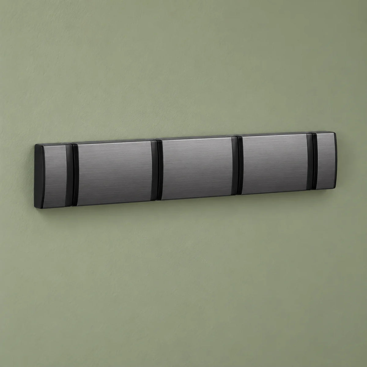 Petit porte-manteau mural gris en position fermée sur fond vert sauge
