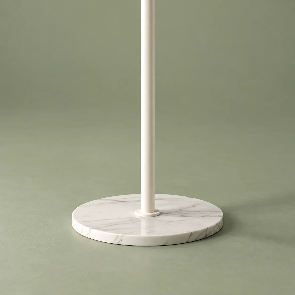 Gros plan sur la base ronde blanche à veinage gris clair et la tige métallique blanche du porte-manteau sur fond vert sauge
