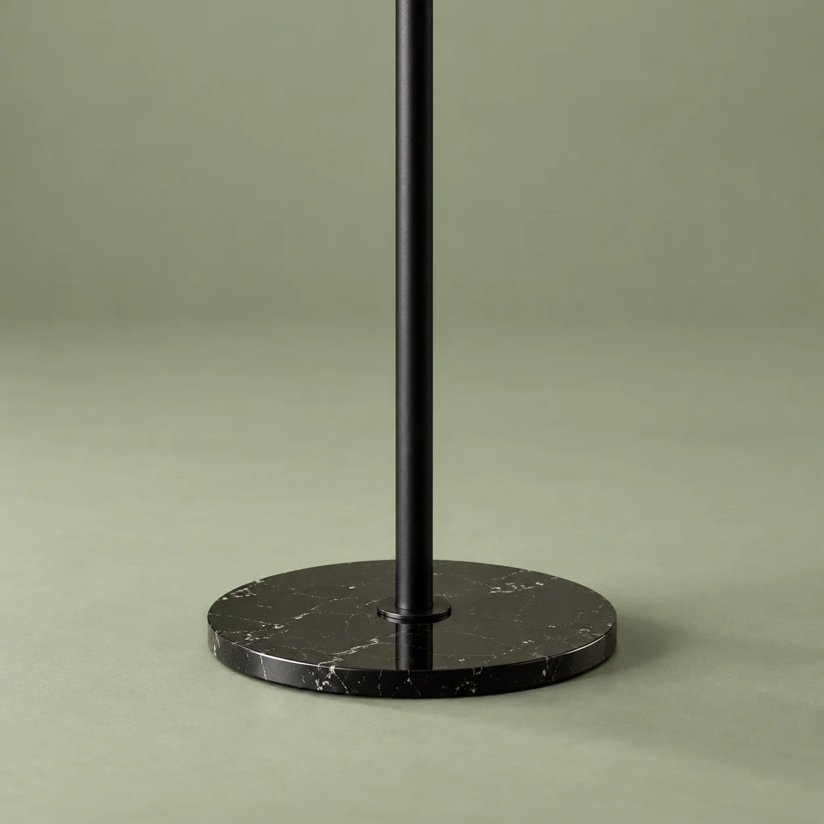Gros plan sur la base ronde noire à veinage clair et la tige métallique noire du porte-manteau sur fond vert sauge