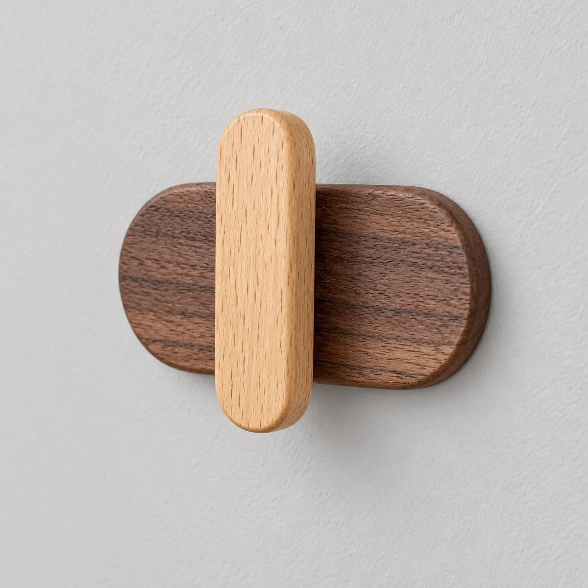Vue rapprochée de la patère capsule claire montrant le relief du crochet en bois clair sur la base foncée