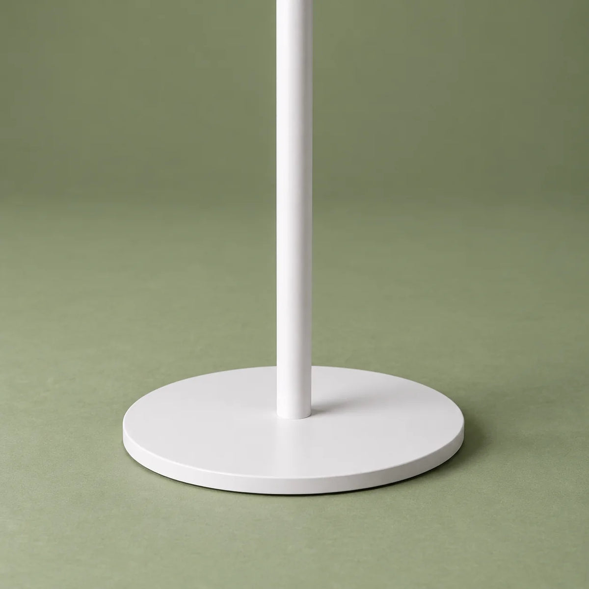 Détail de la base circulaire blanche et du pied blanc sur fond vert sauge