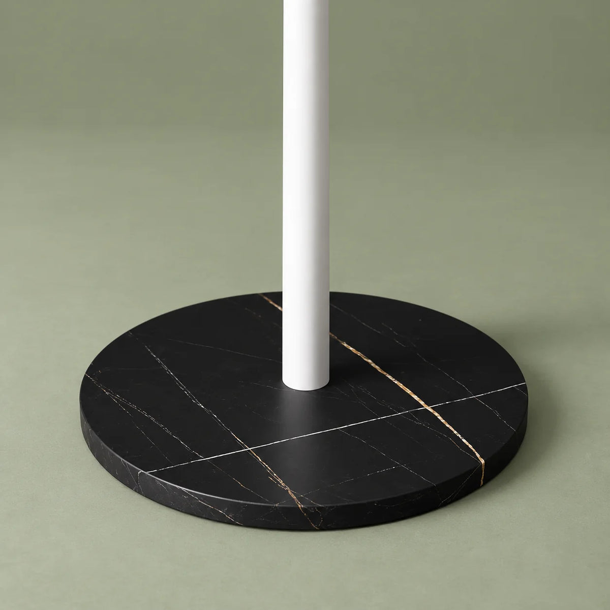 Gros plan de la base circulaire noire marbrée et du pied blanc sur fond vert sauge