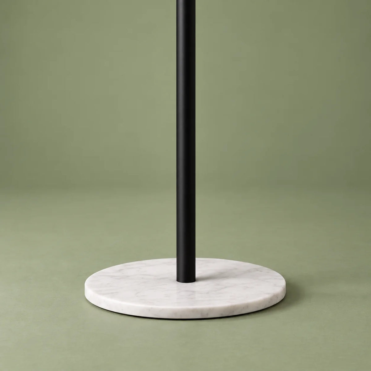 Détail de la base ronde blanche et du pied noir du porte-manteau arbre sur fond vert sauge