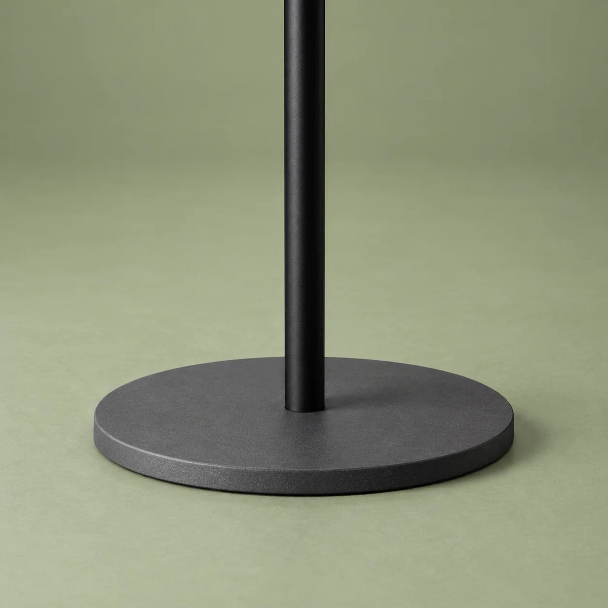 Détail de la base circulaire gris anthracite du porte-manteau arbre noir sur fond vert sauge