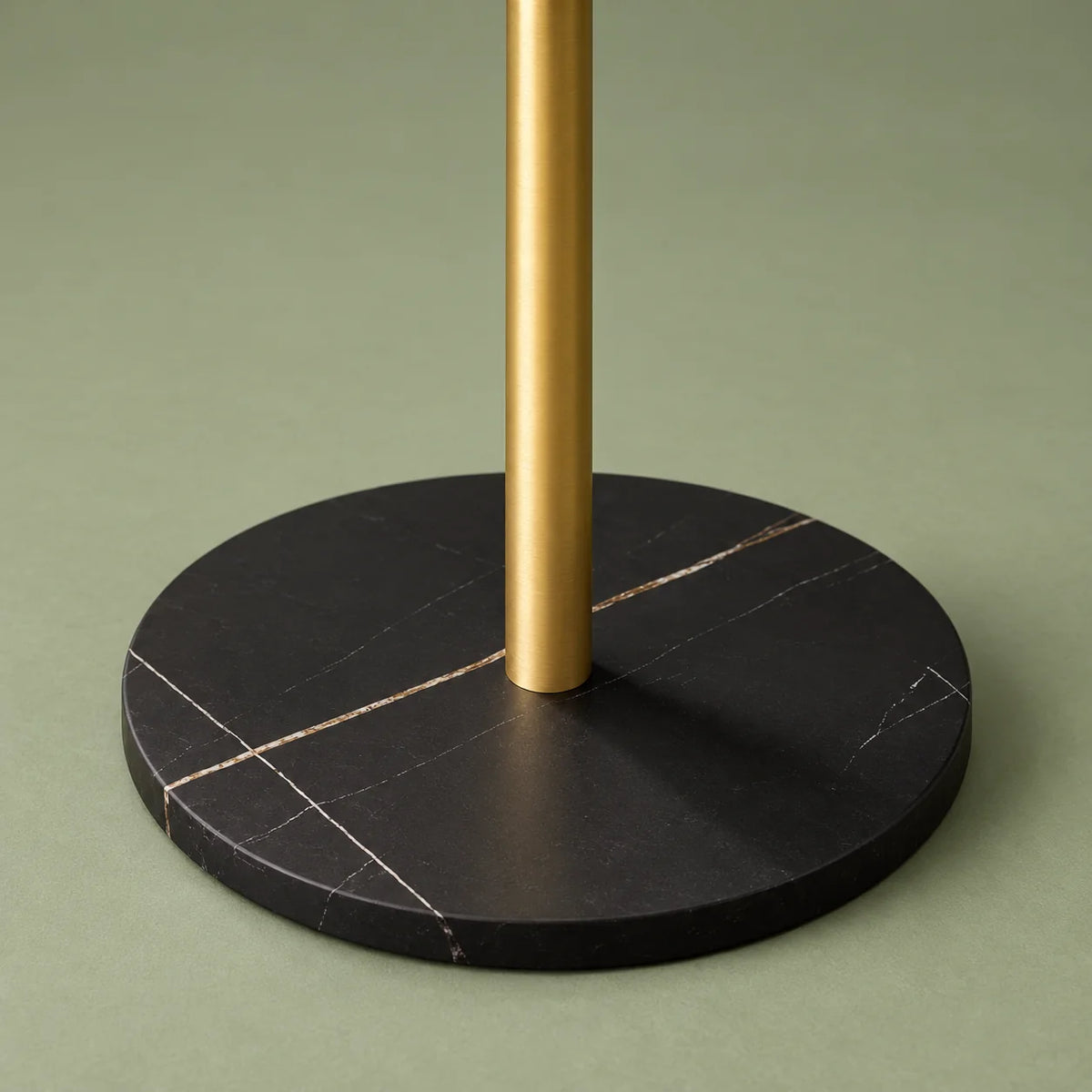 Gros plan de la base circulaire noire marbrée et du pied doré sur fond vert sauge