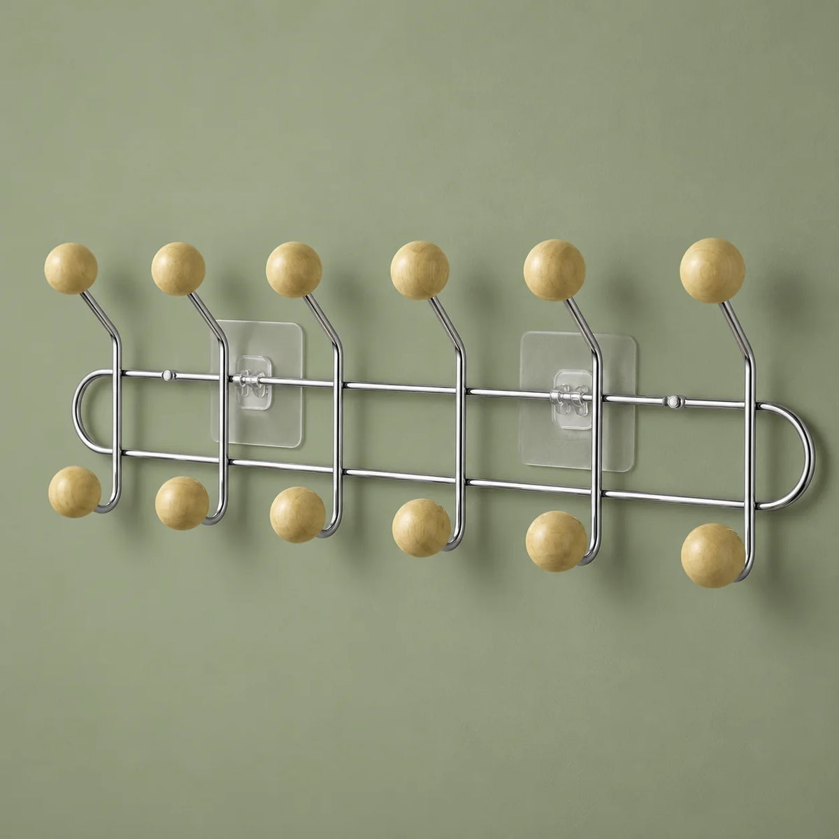 Vue légèrement oblique des six bras chromés et douze boules bois jaune crème sur fond vert