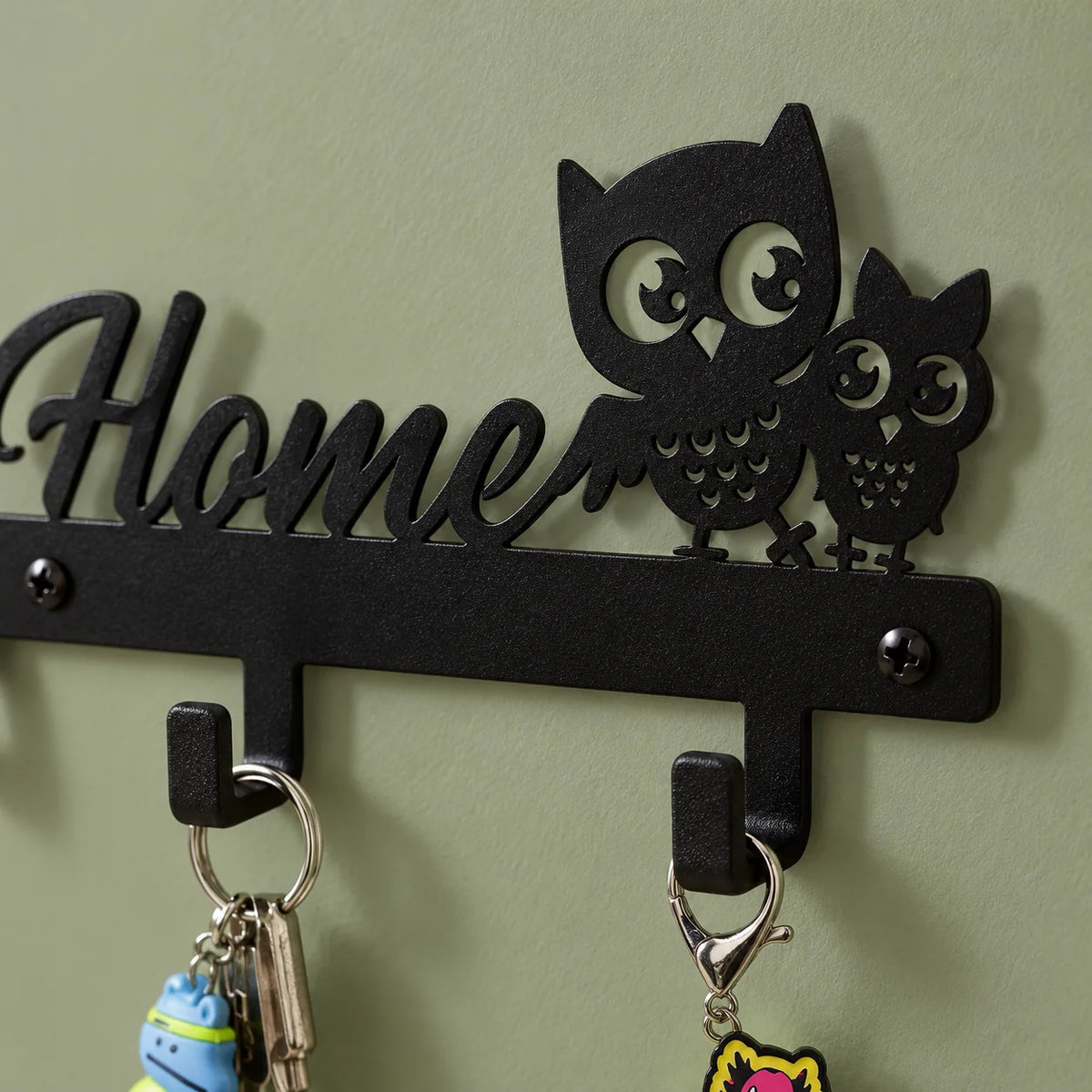 Détail de la découpe des deux hiboux et des fixations du porte-clés Home sur fond vert sauge