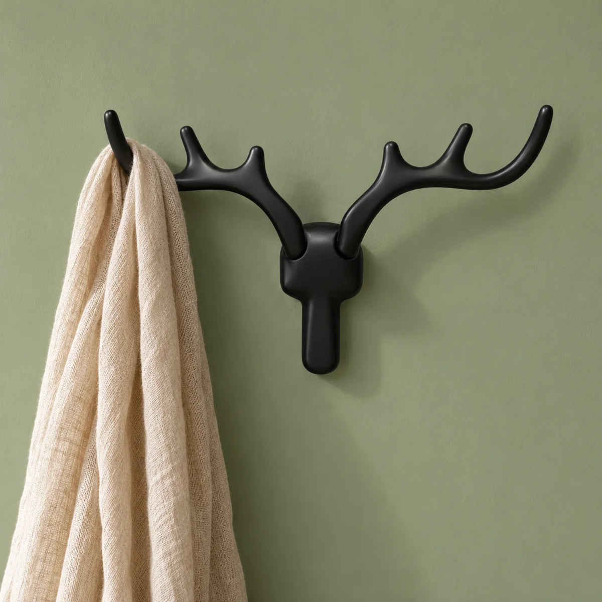 Patère cerf noire portant une écharpe sur mur vert sauge