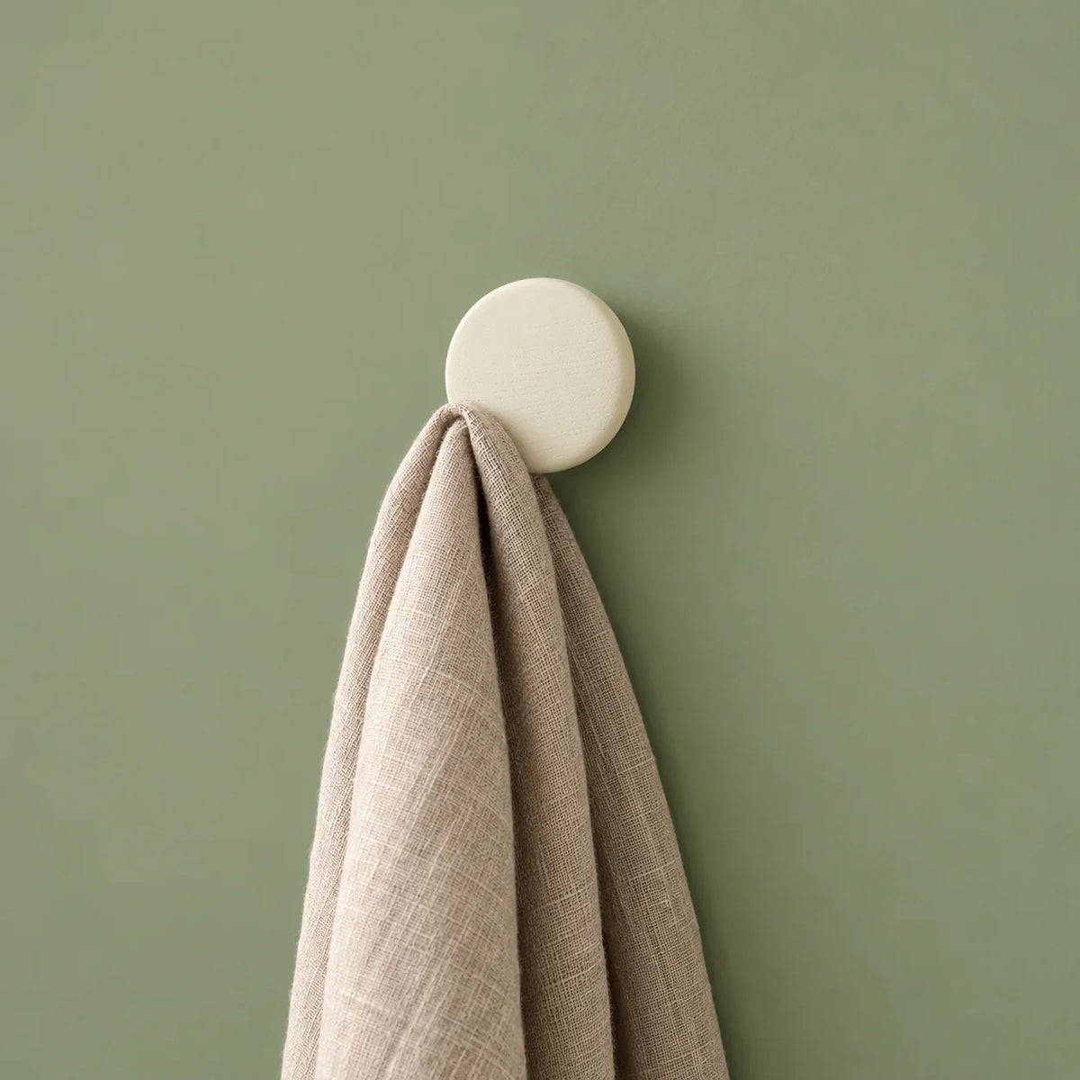 Patère ronde blanche portant une écharpe sur mur vert sauge