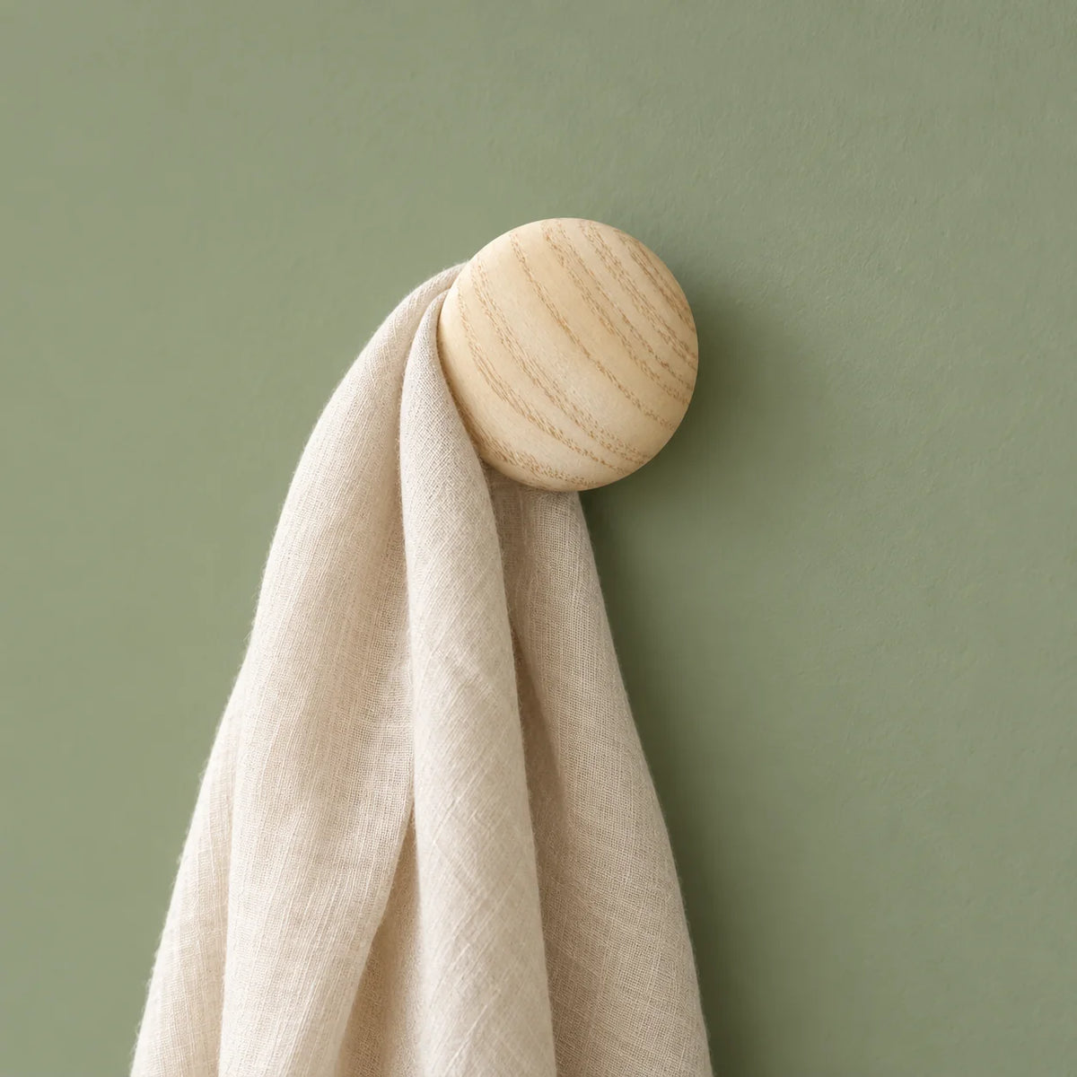 Patère ronde en bois clair portant une écharpe sur mur vert sauge