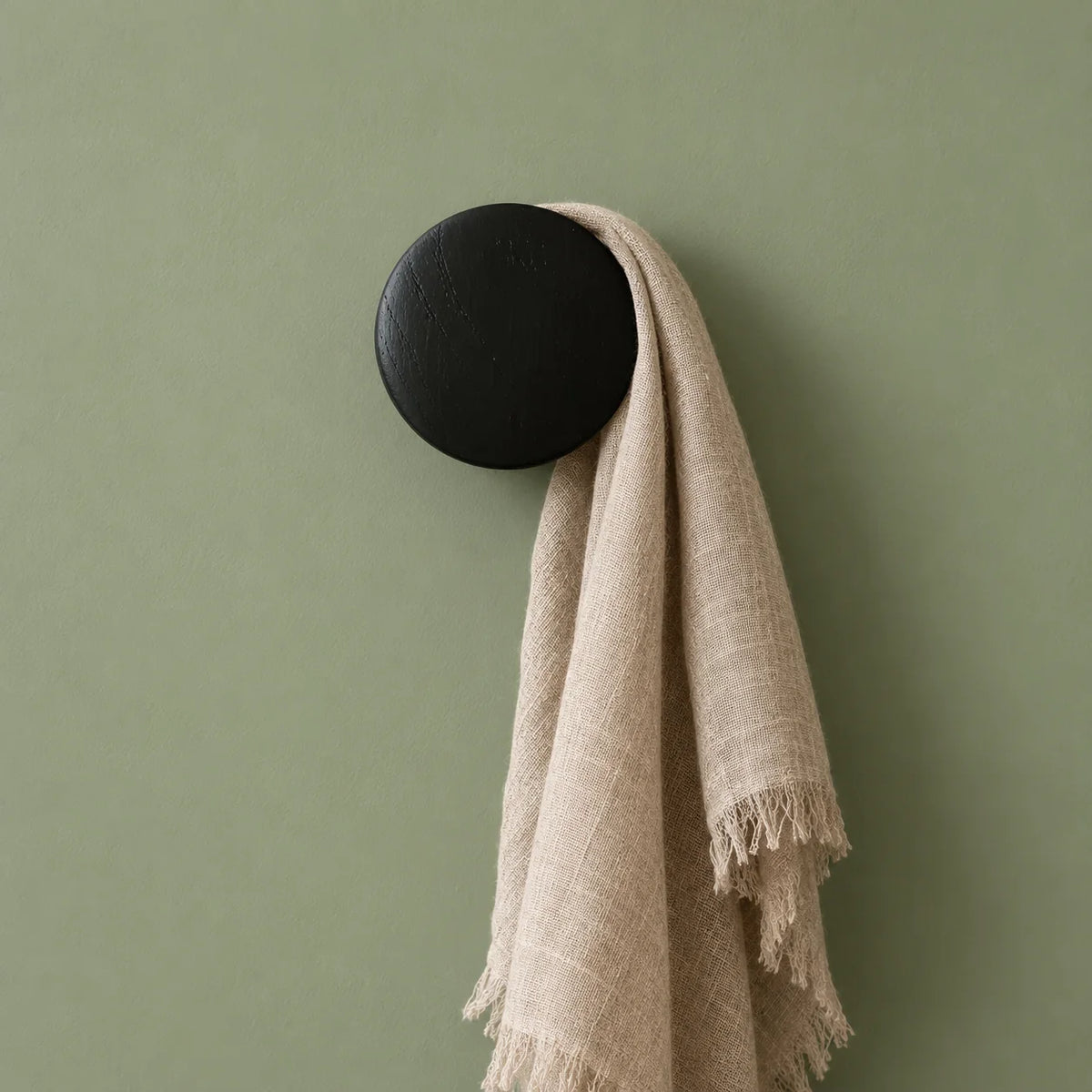 Patère ronde noire portant une écharpe sur mur vert sauge