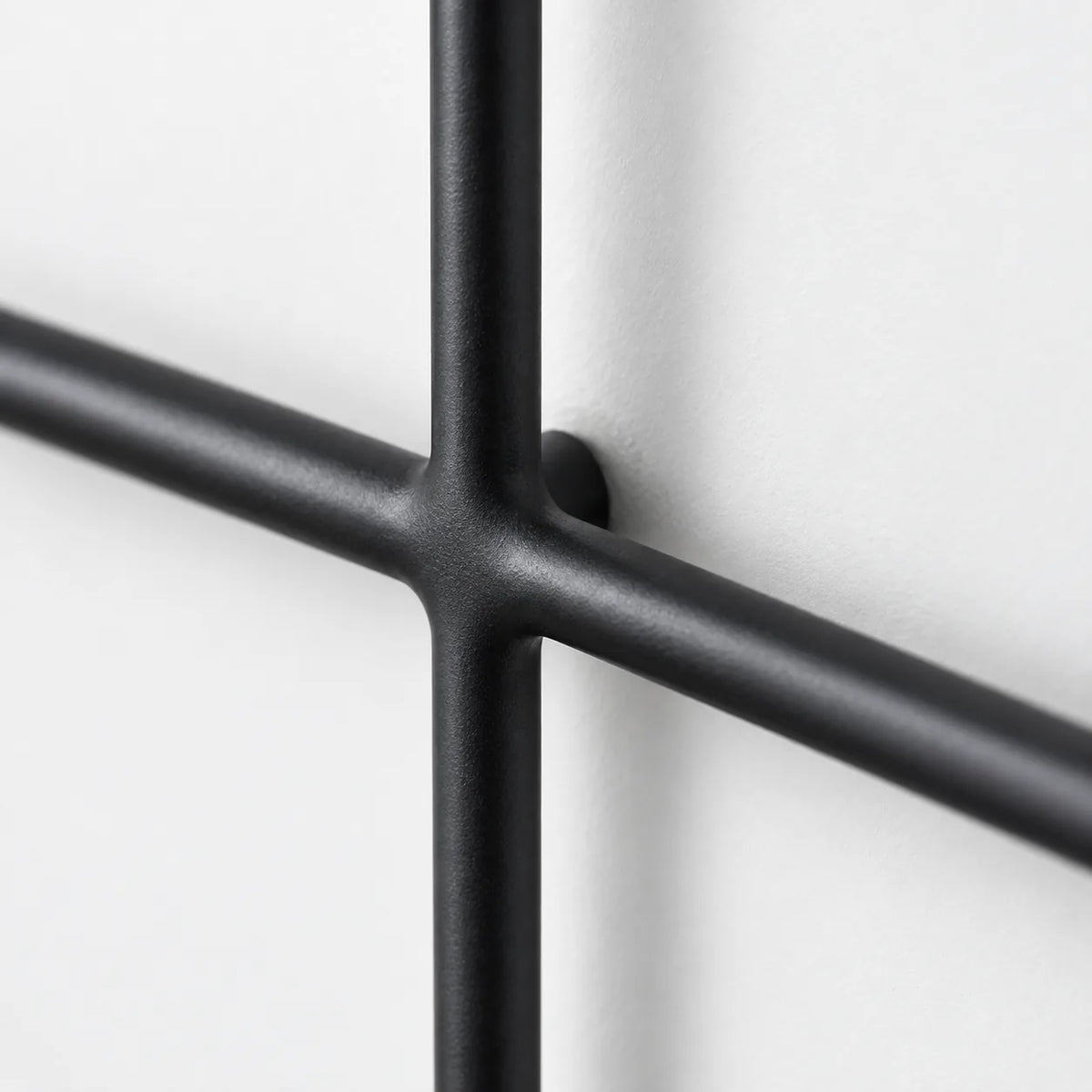 Detail du croisement des barres noires et de la fixation murale du porte manteau