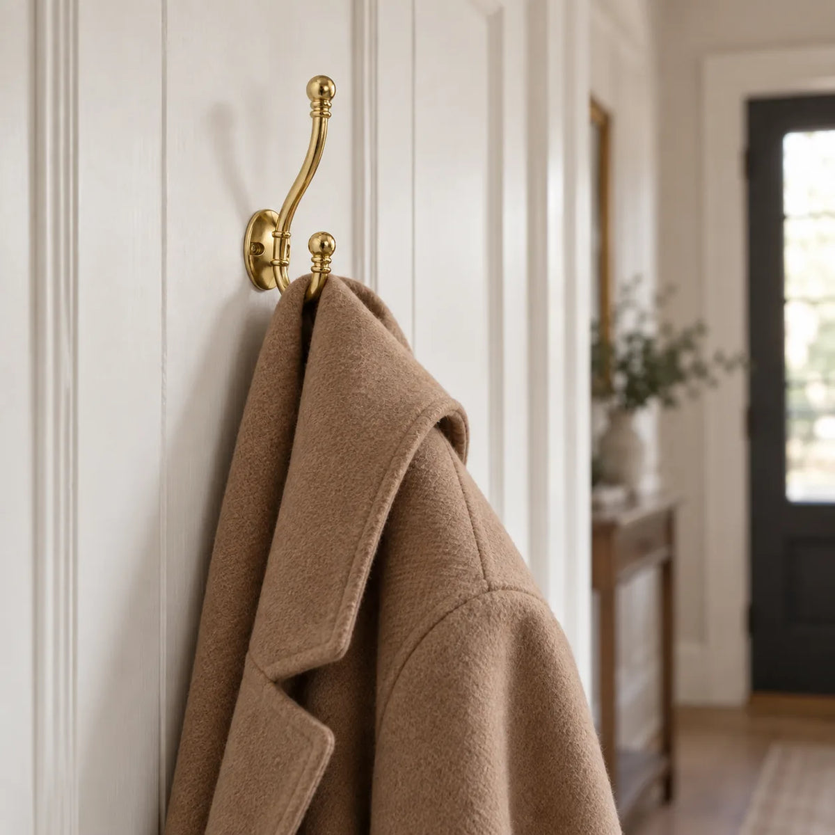 Patere crochet ancien doree vissee sur boiserie blanche avec manteau en laine camel