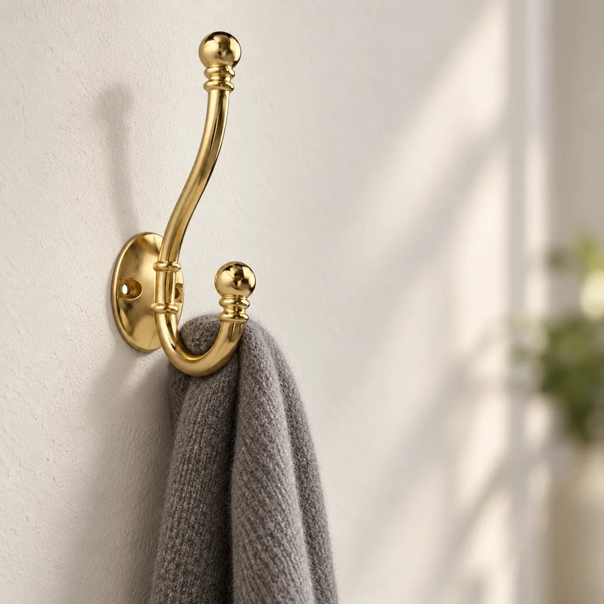 Patere crochet ancien doree vissee sur un mur clair avec une echarpe en laine grise