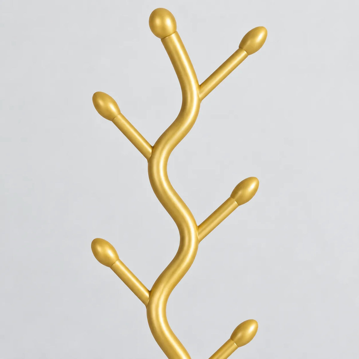 Gros plan sur les branches dorées et embouts arrondis du porte manteau sur pied