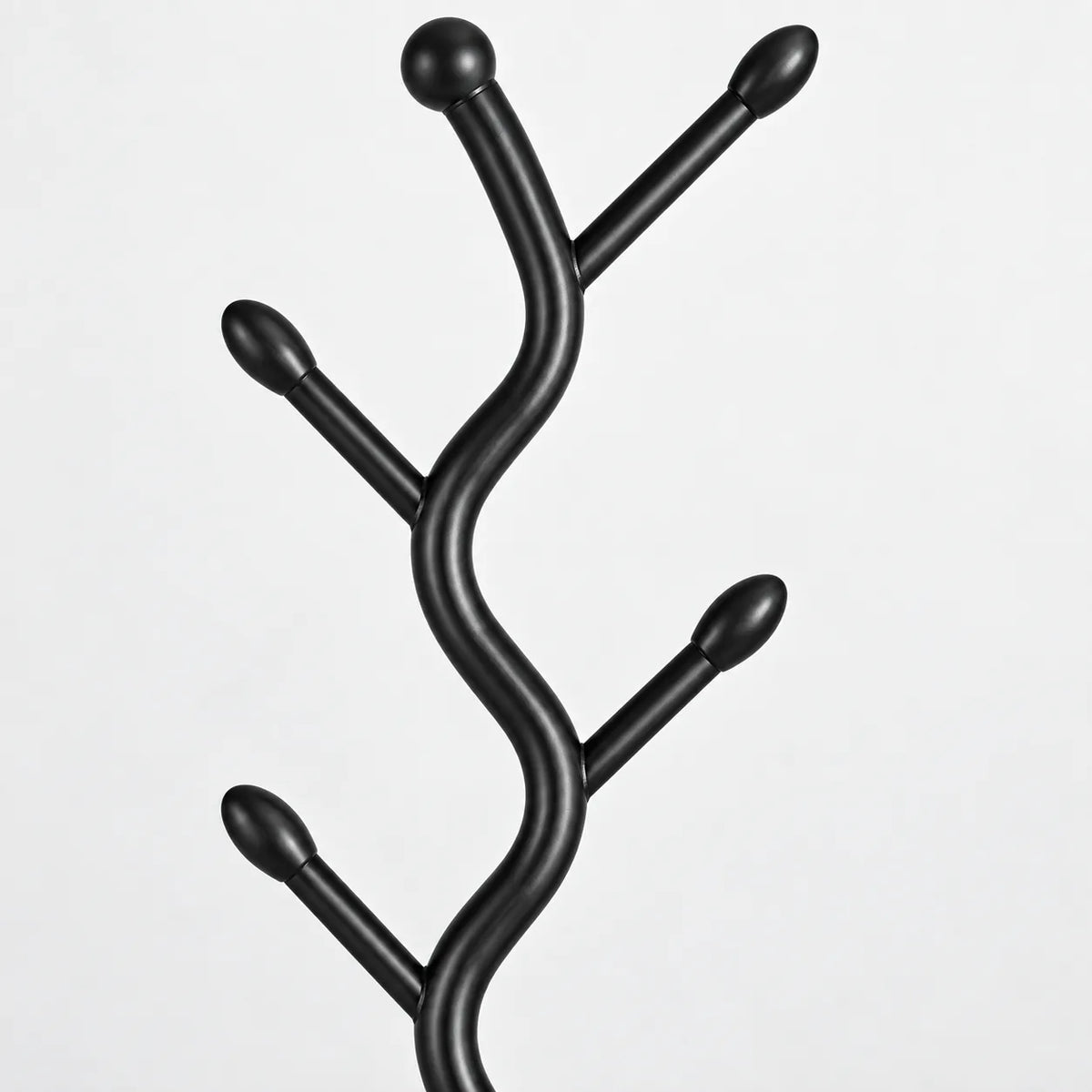 Gros plan sur les branches noires et embouts arrondis du porte manteau sur pied
